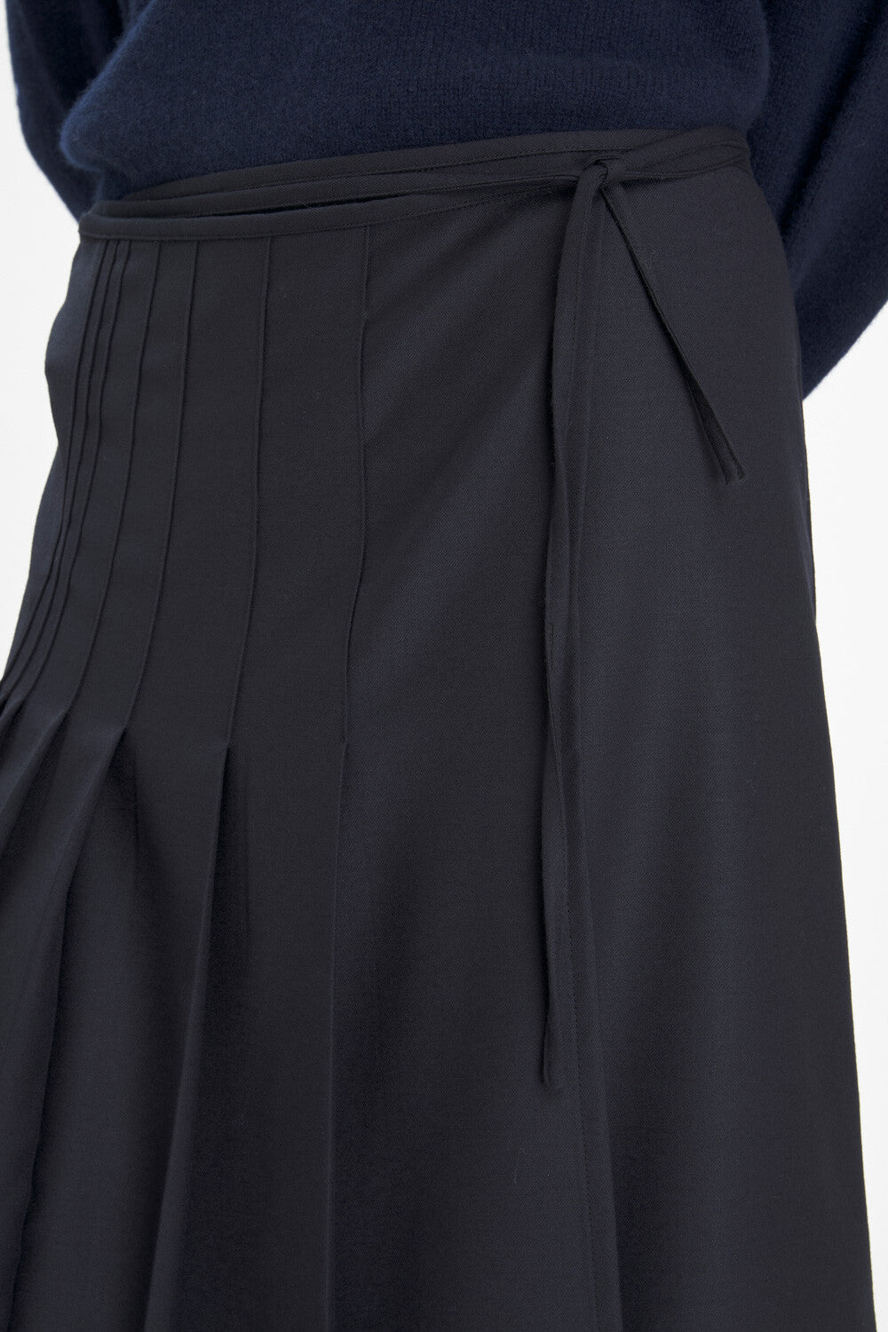 Close-up of a dark navy pleated skirt with a matching tie belt, paired with a navy top against a light gray background.
