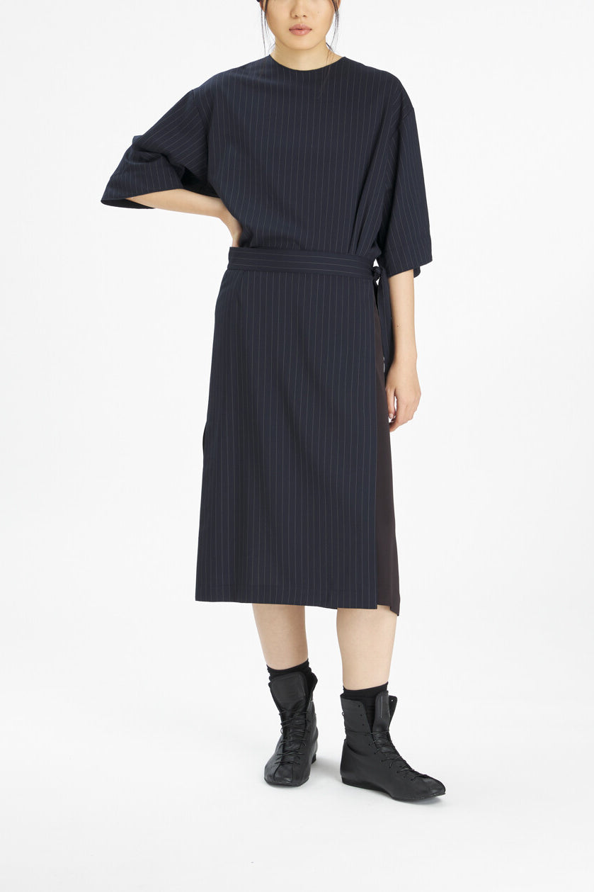 A model wearing a dark navy blue ribbed midi dress with a tie waist and elbow-length sleeves, paired with black ankle boots, against a plain white studio background.