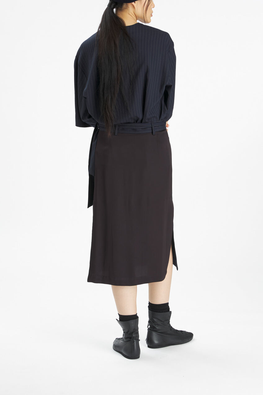A model shown from the back wearing a dark navy blue pinstriped wrap-style top and a dark brown midi skirt with side slits, paired with black ankle boots, against a plain white studio background.