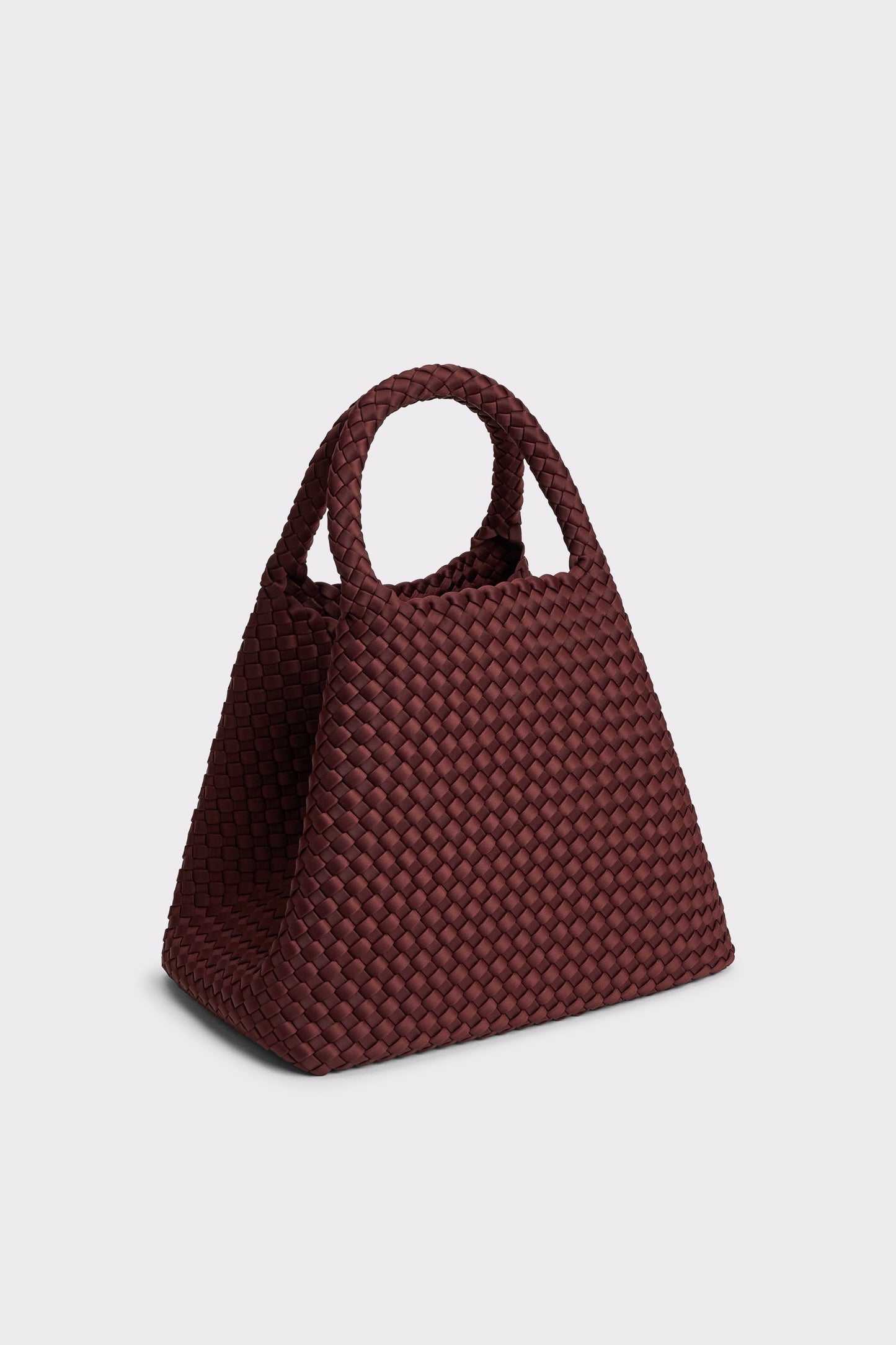A small woven handbag in a deep burgundy brown, featuring a structured basketweave pattern and two top handles, set against a plain light gray background.