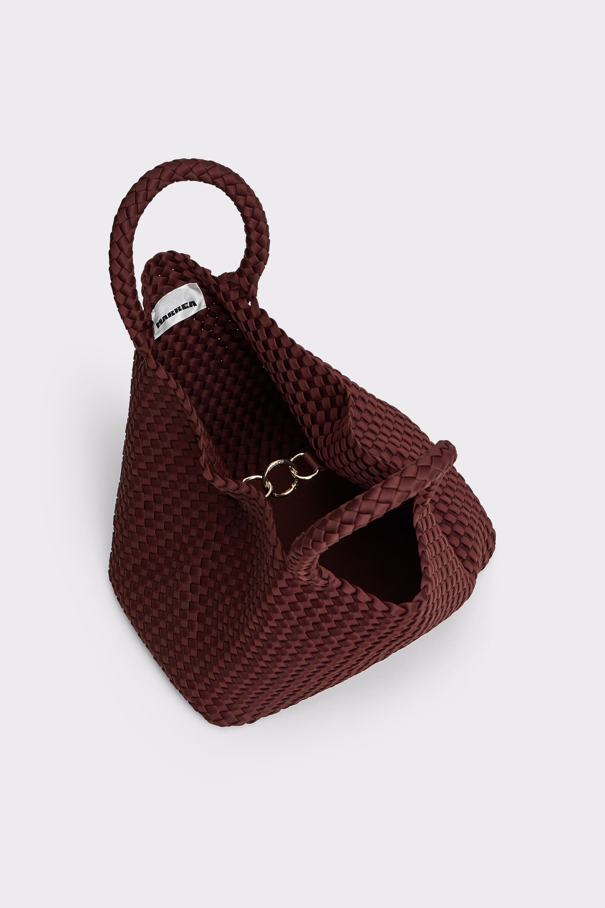 A dark burgundy woven leather handbag with a single top handle and a small silver-tone ring detail, shown on a light gray background.