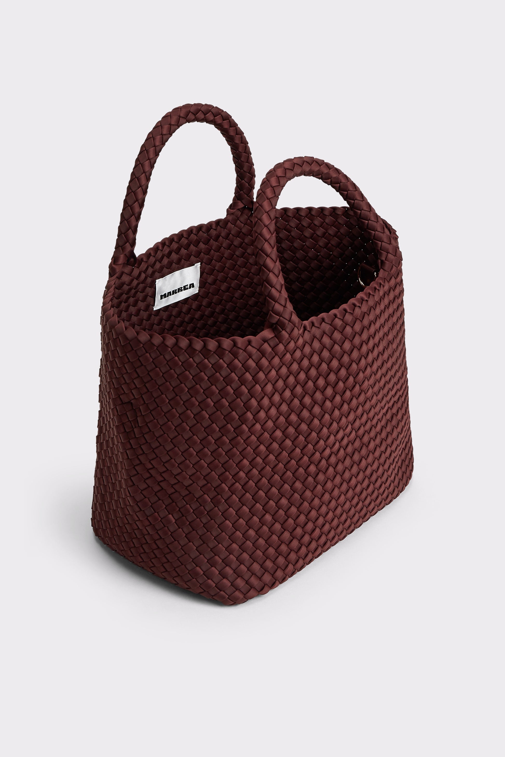 A dark burgundy woven basket bag with two top handles and a small white brand tag, shown on a light gray background.
