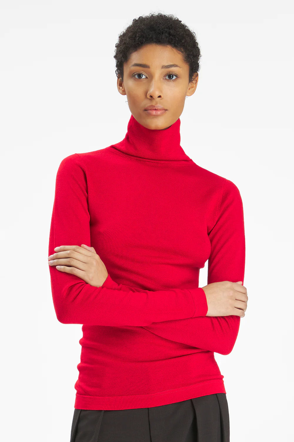 A model wearing a bright red long-sleeve turtleneck sweater, paired with dark gray pants, against a plain white studio background.