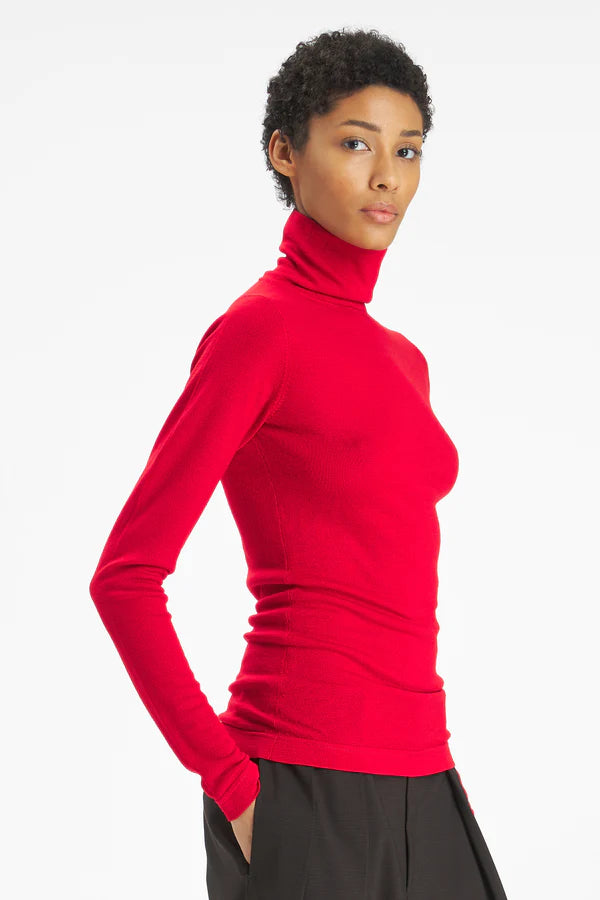 A woman modeling a bright red long-sleeve turtleneck top against a clean white studio background.