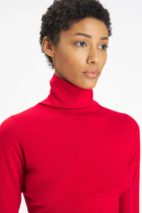 A close-up shot of a model wearing a bright red, long-sleeve mock neck turtleneck sweater against a plain white background.