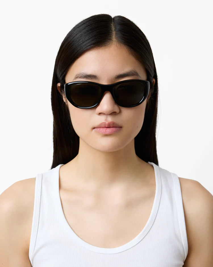 Woman wearing black sunglasses and a white tank top on a white background