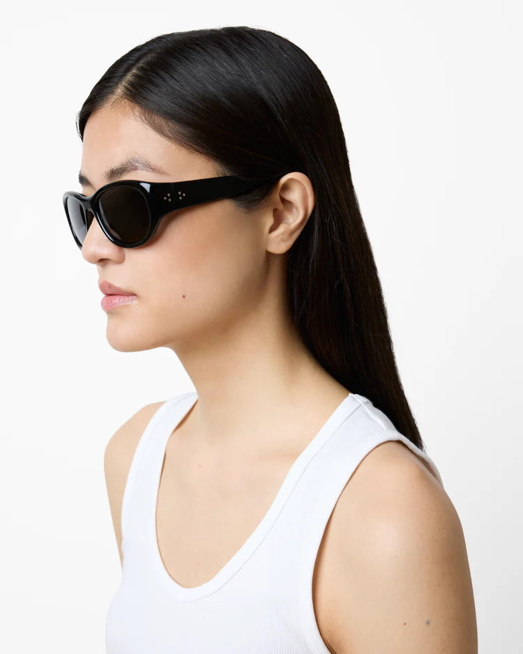 Woman wearing black sunglasses and a white tank top on a plain background