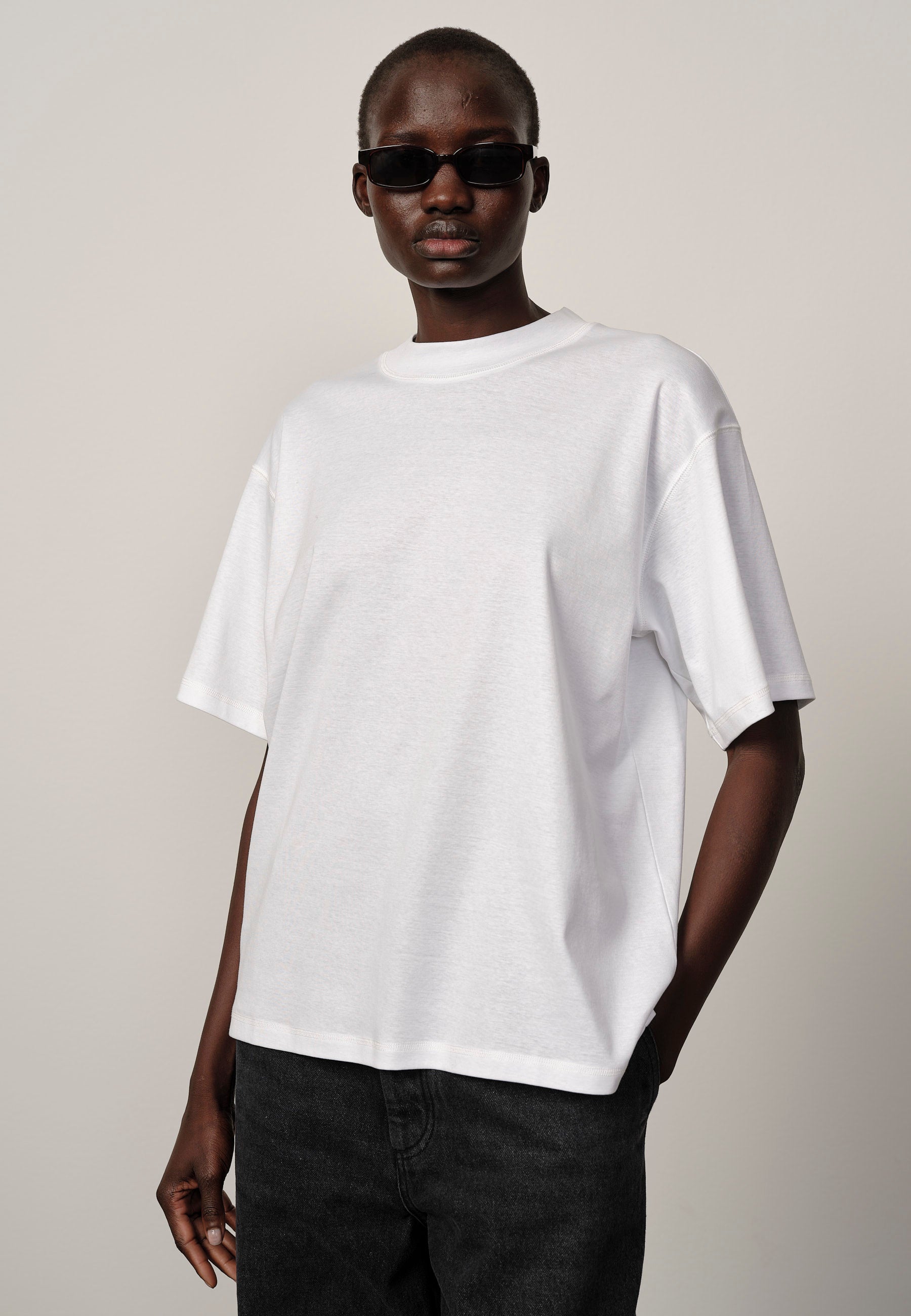 Person wearing a plain white t-shirt and dark sunglasses on a neutral background