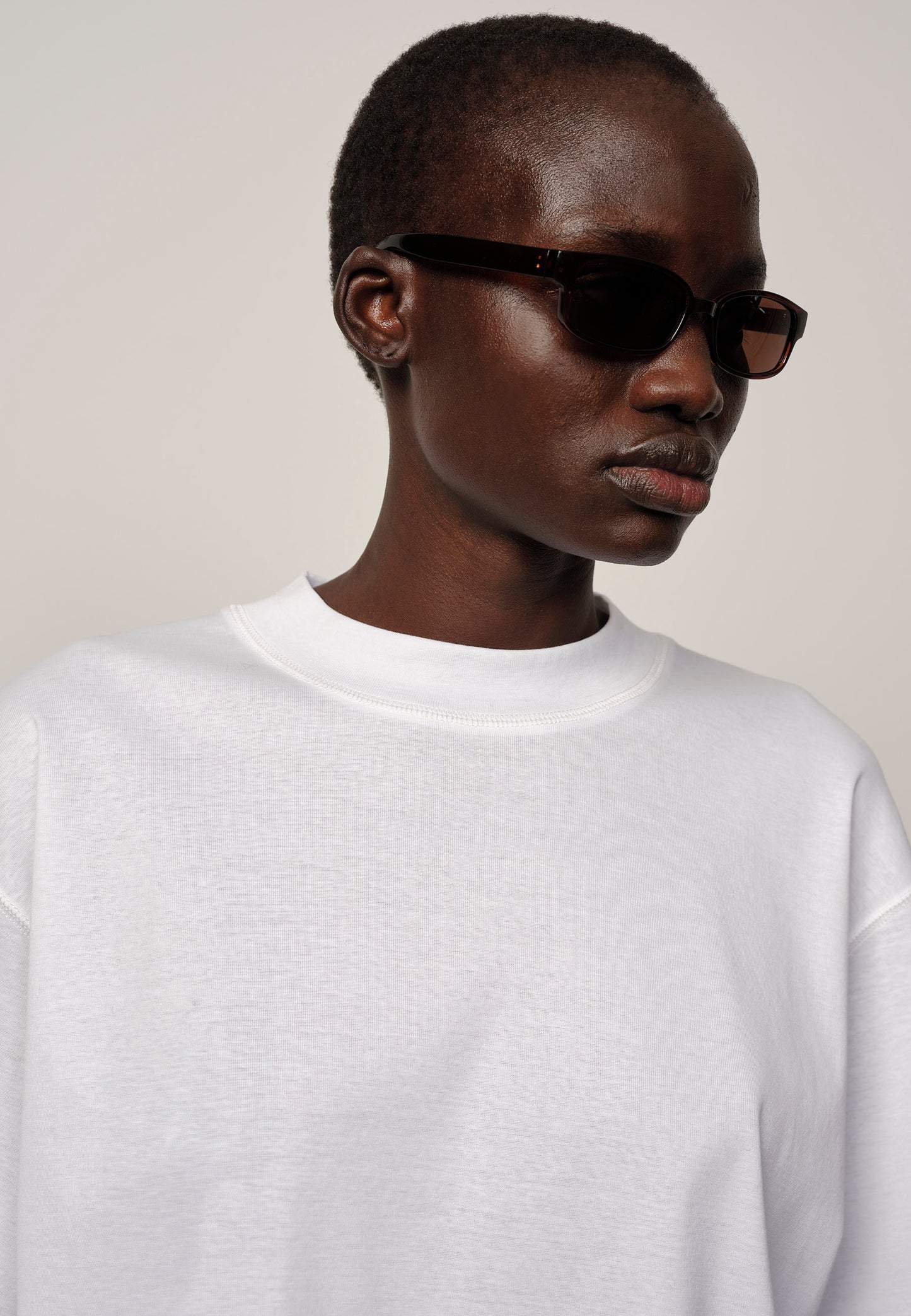 Person wearing black sunglasses and a white shirt against a plain background