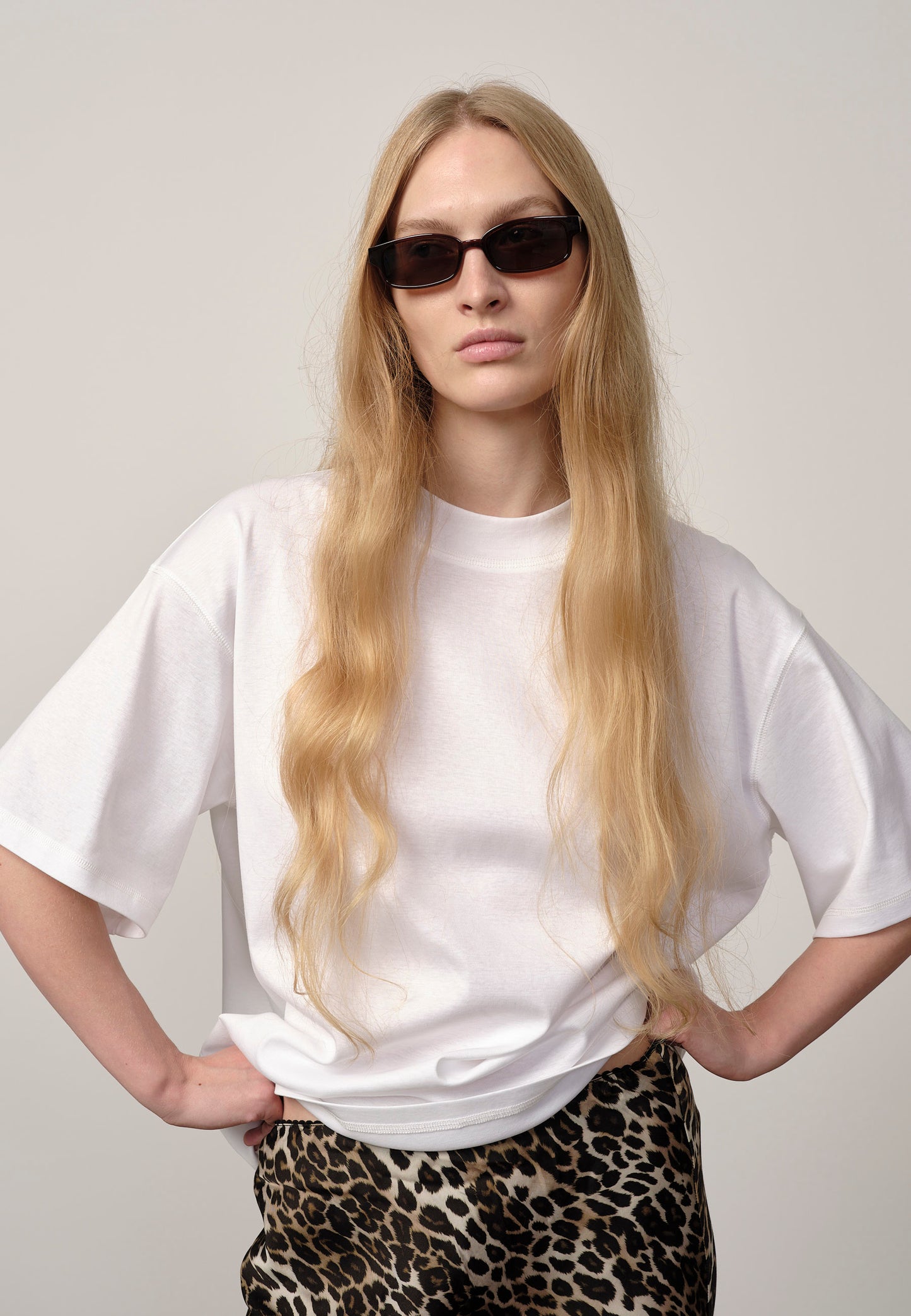 Person wearing a white t-shirt and leopard print pants with sunglasses on a plain background