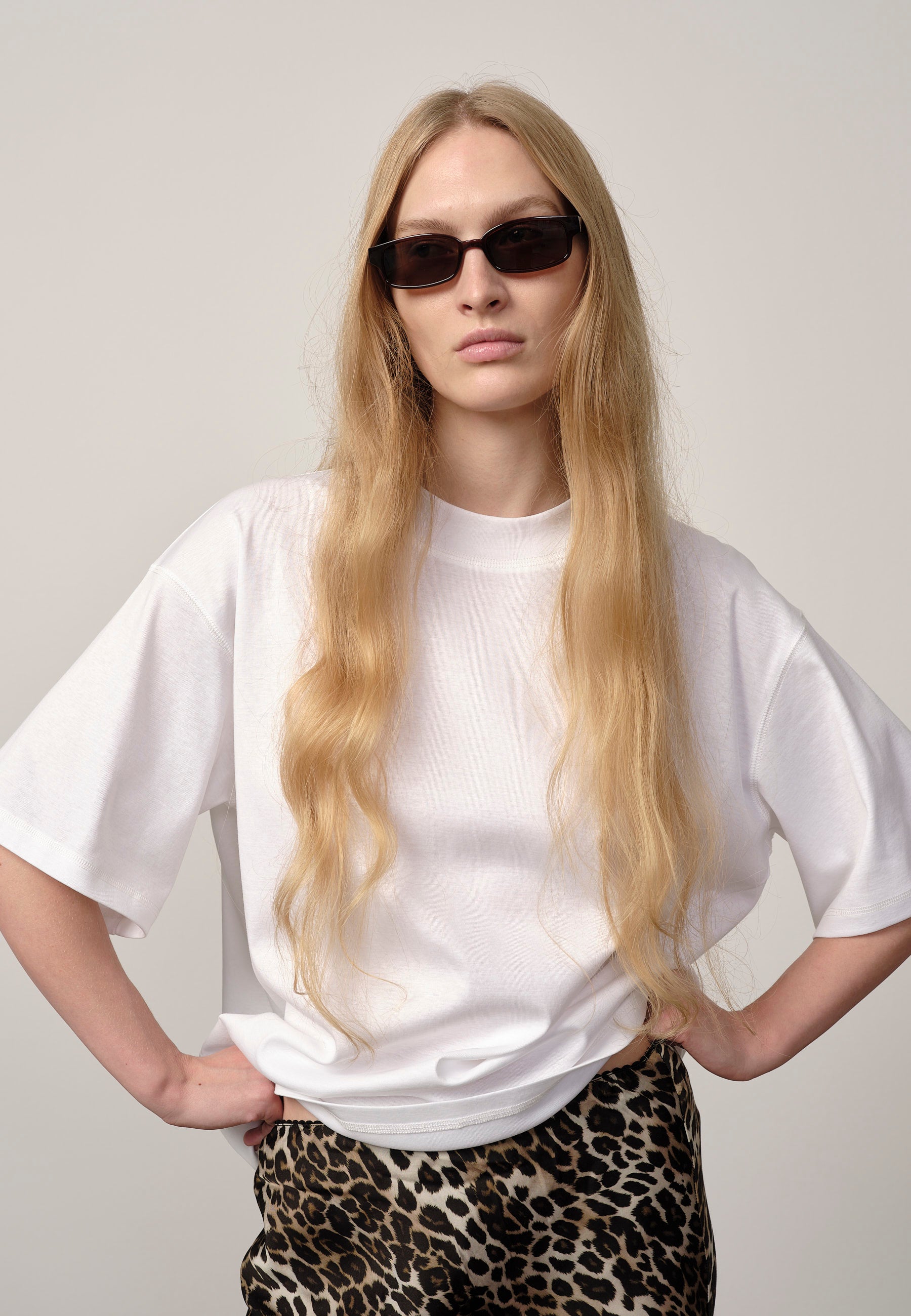 Person wearing a white t-shirt and leopard print pants with sunglasses on a plain background