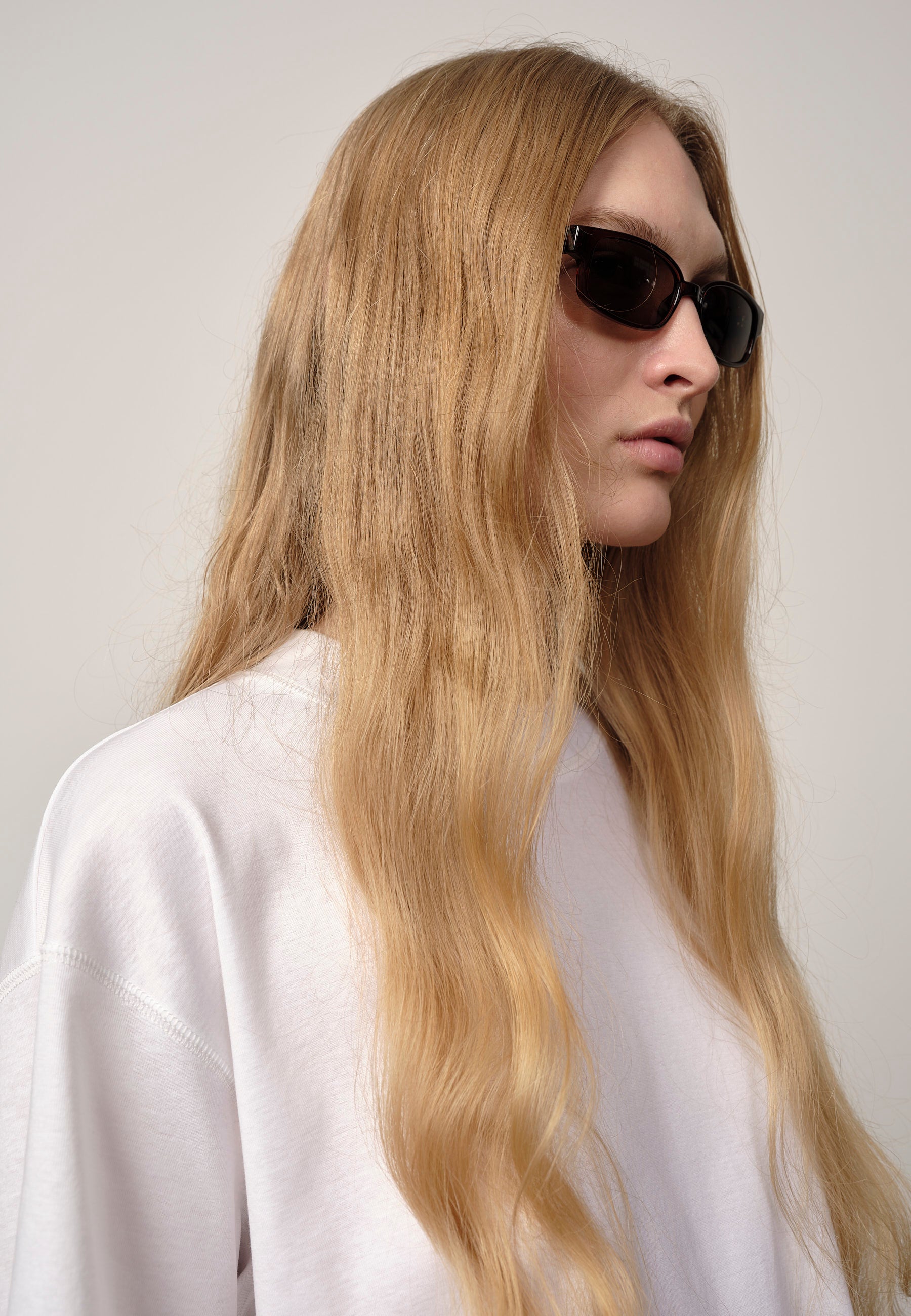 Woman with long blonde hair wearing sunglasses against a plain background