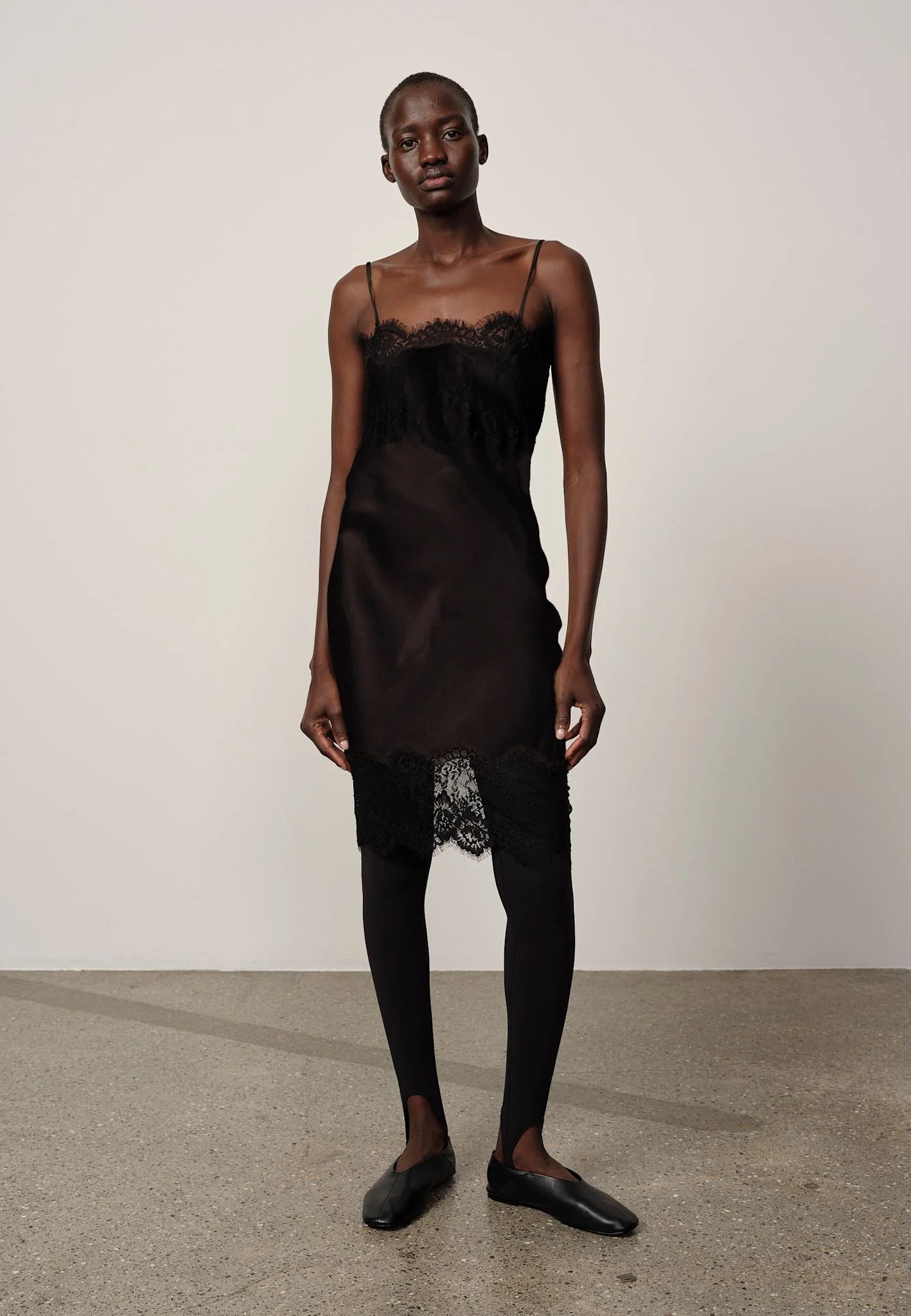 Person wearing a black slip dress with lace details on a plain background