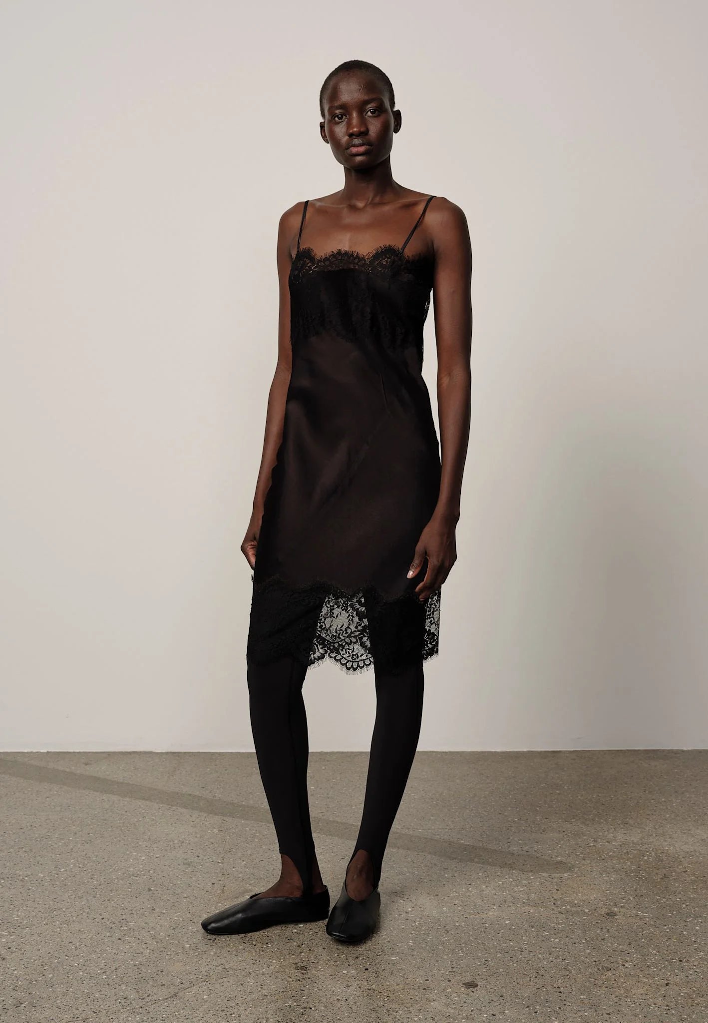 Model wearing a black slip dress with lace details against a plain background