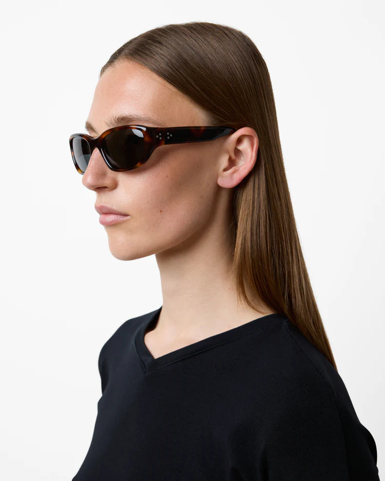 Person wearing tortoiseshell sunglasses with a plain background