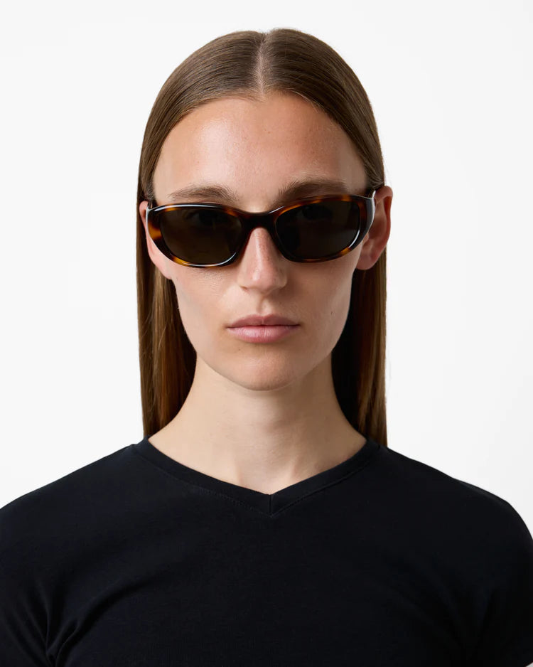 Person wearing tortoiseshell sunglasses with a plain background