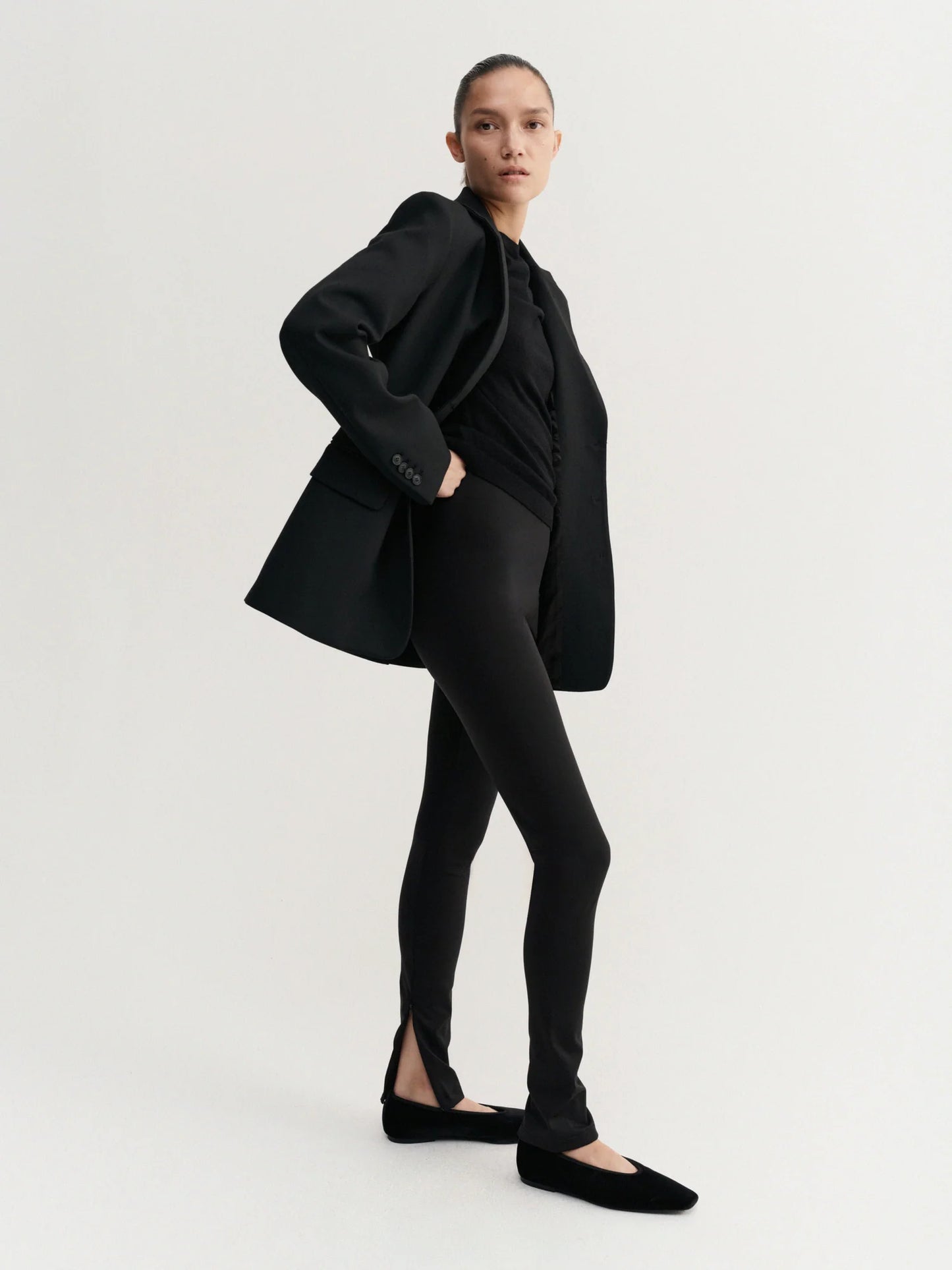 Person wearing a black blazer and leggings on a white background