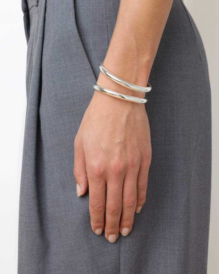 Silver bracelets on a wrist with a gray dress background