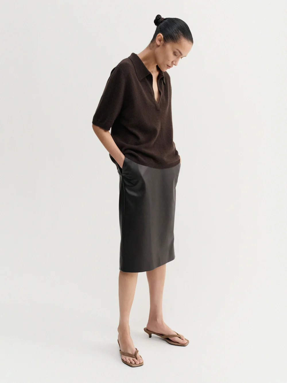 Person wearing a brown sweater and black leather skirt on a white background