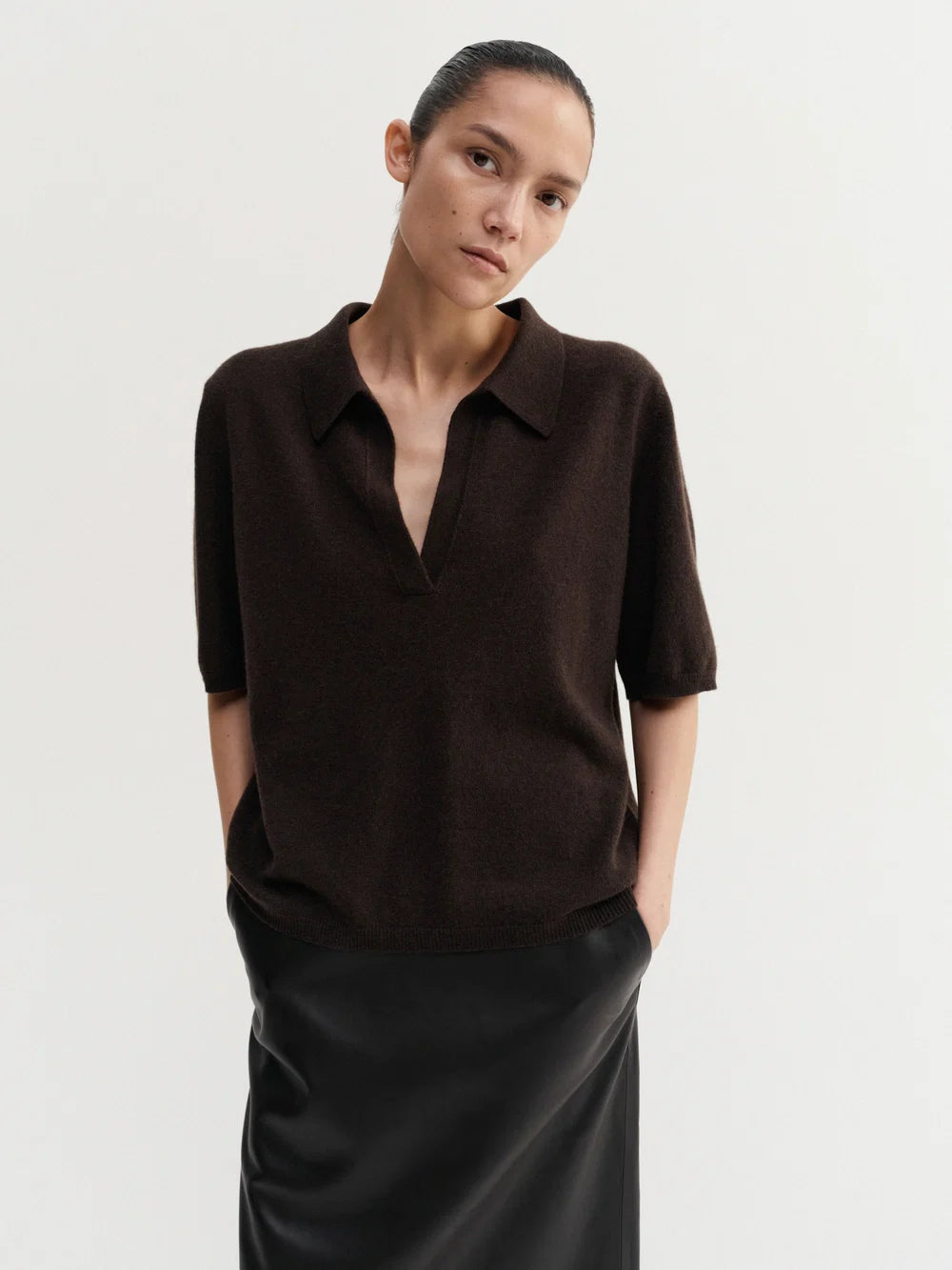 Person wearing a brown short-sleeve shirt and black pants on a light gray background