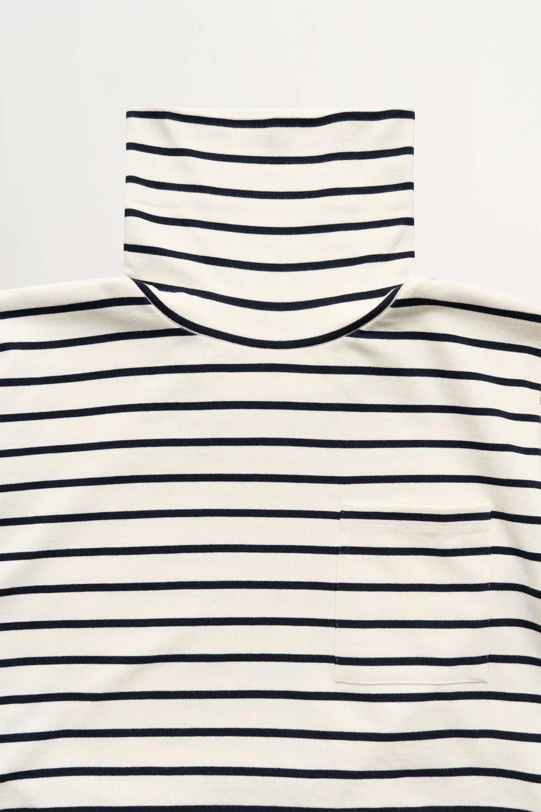 A close-up of a striped turtleneck sweater with horizontal navy blue stripes on an off-white base, featuring a small chest pocket on the wearer's left side.