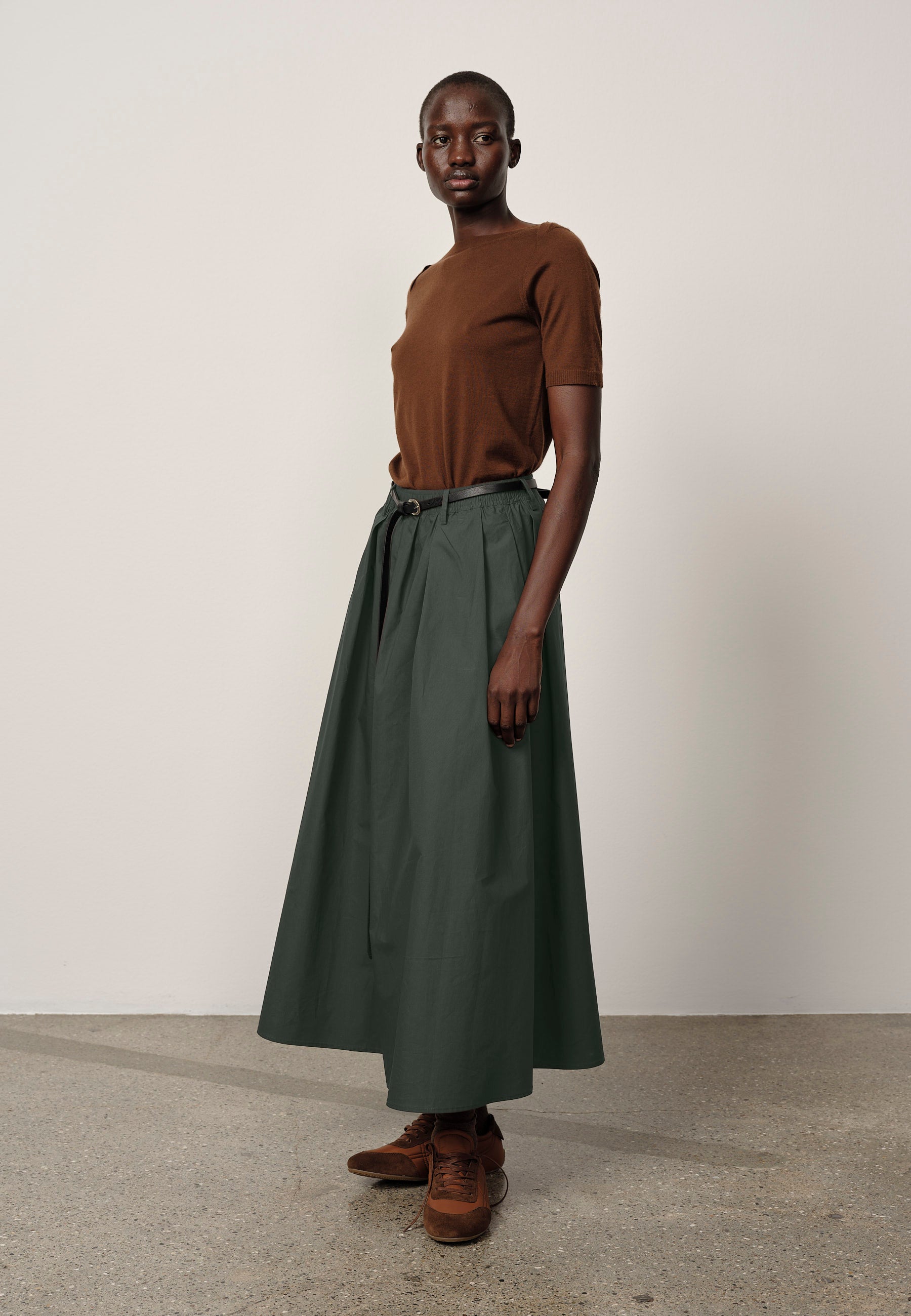 Person wearing a brown top and green skirt on a plain background