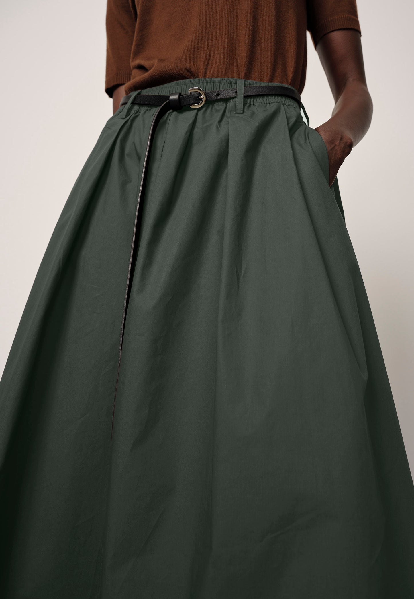 Person wearing a long green skirt with a plain background