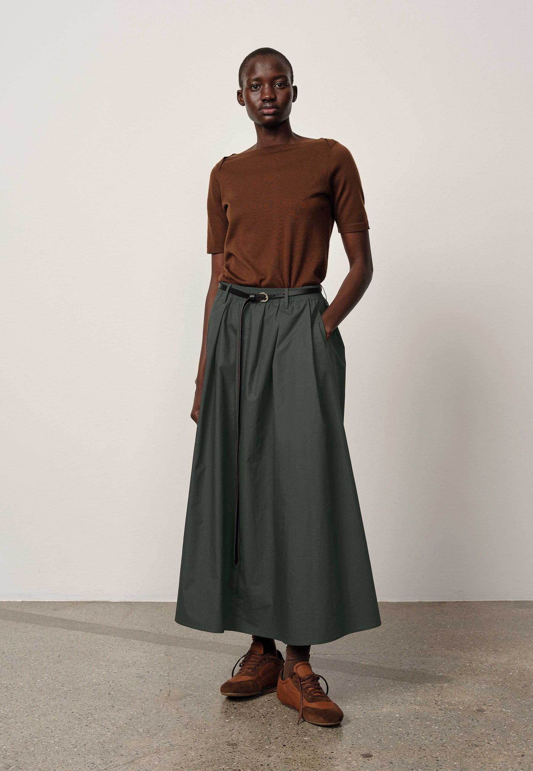 Person wearing a brown top and green skirt against a plain background