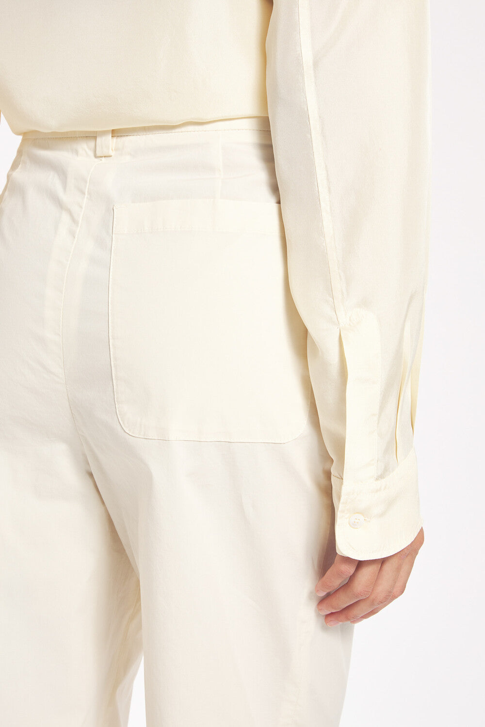Person wearing a light-colored outfit with a focus on pants and shirt on a white background