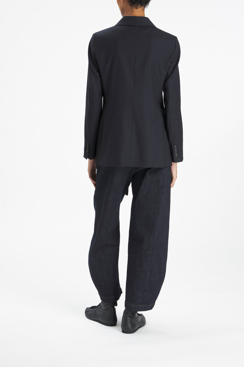 A model shown from the back wearing a dark navy blue blazer and matching wide-leg trousers, paired with black shoes, against a plain white studio background.
