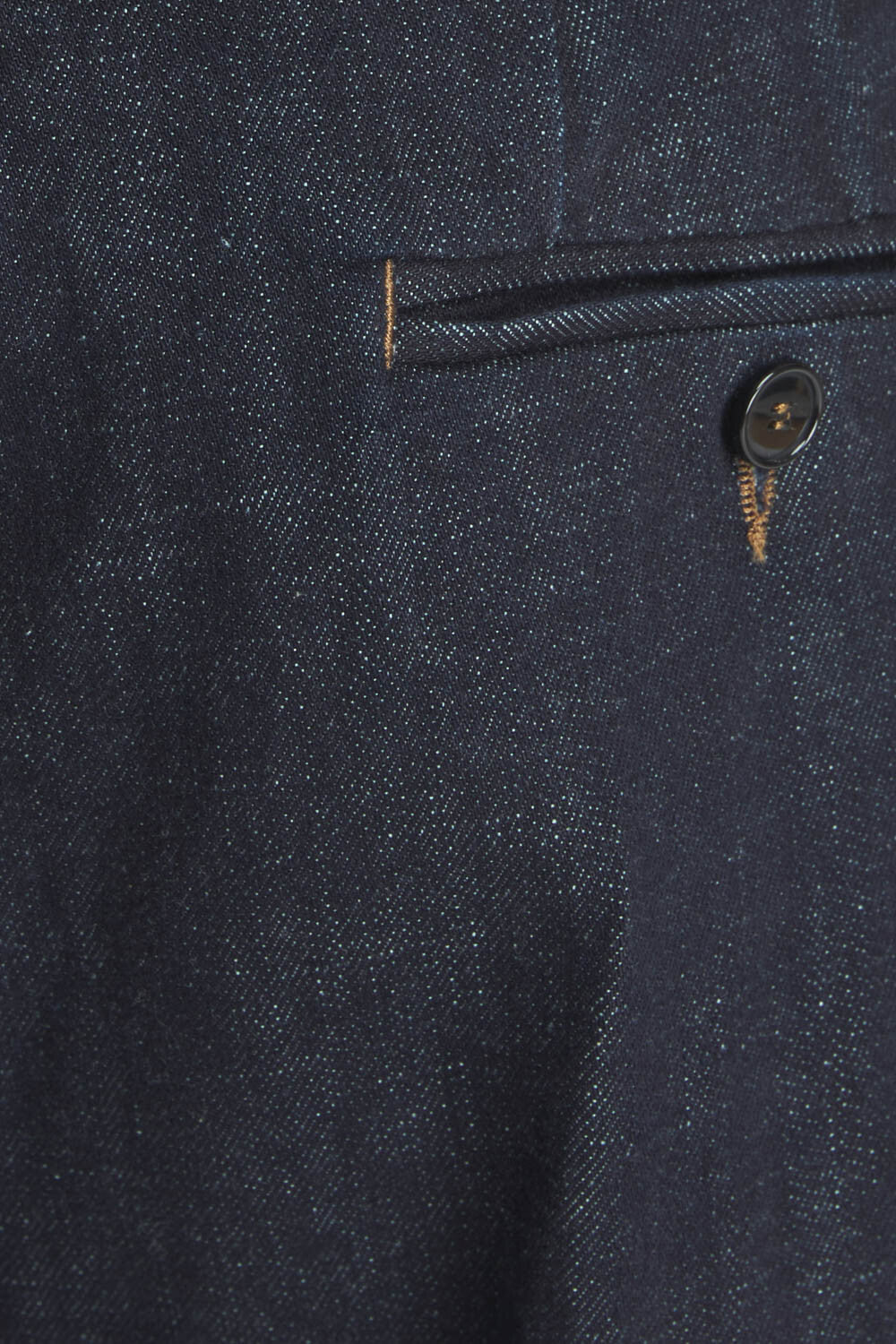 Close-up of dark indigo denim fabric showing a pocket with contrast stitching and a dark button.