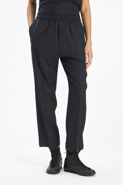 A model wearing black wide-leg cropped trousers with an elastic waistband, paired with black sneakers, shown from the waist down on a white studio background.