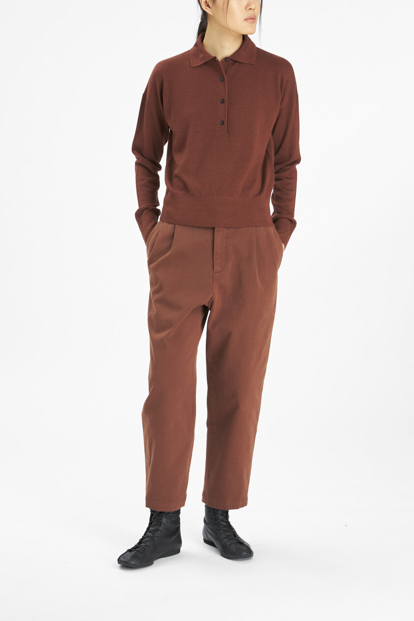 A model wearing a rust-brown knit polo shirt and matching wide-leg trousers, paired with black leather boots, against a plain white studio background.