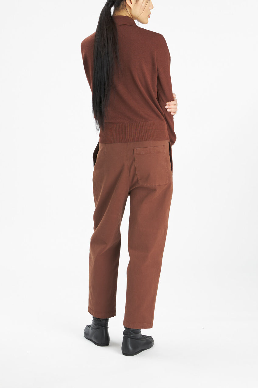 A model shown from the back wearing a rust-brown mock-neck knit top and matching brown pants, paired with black boots, against a plain white studio background.