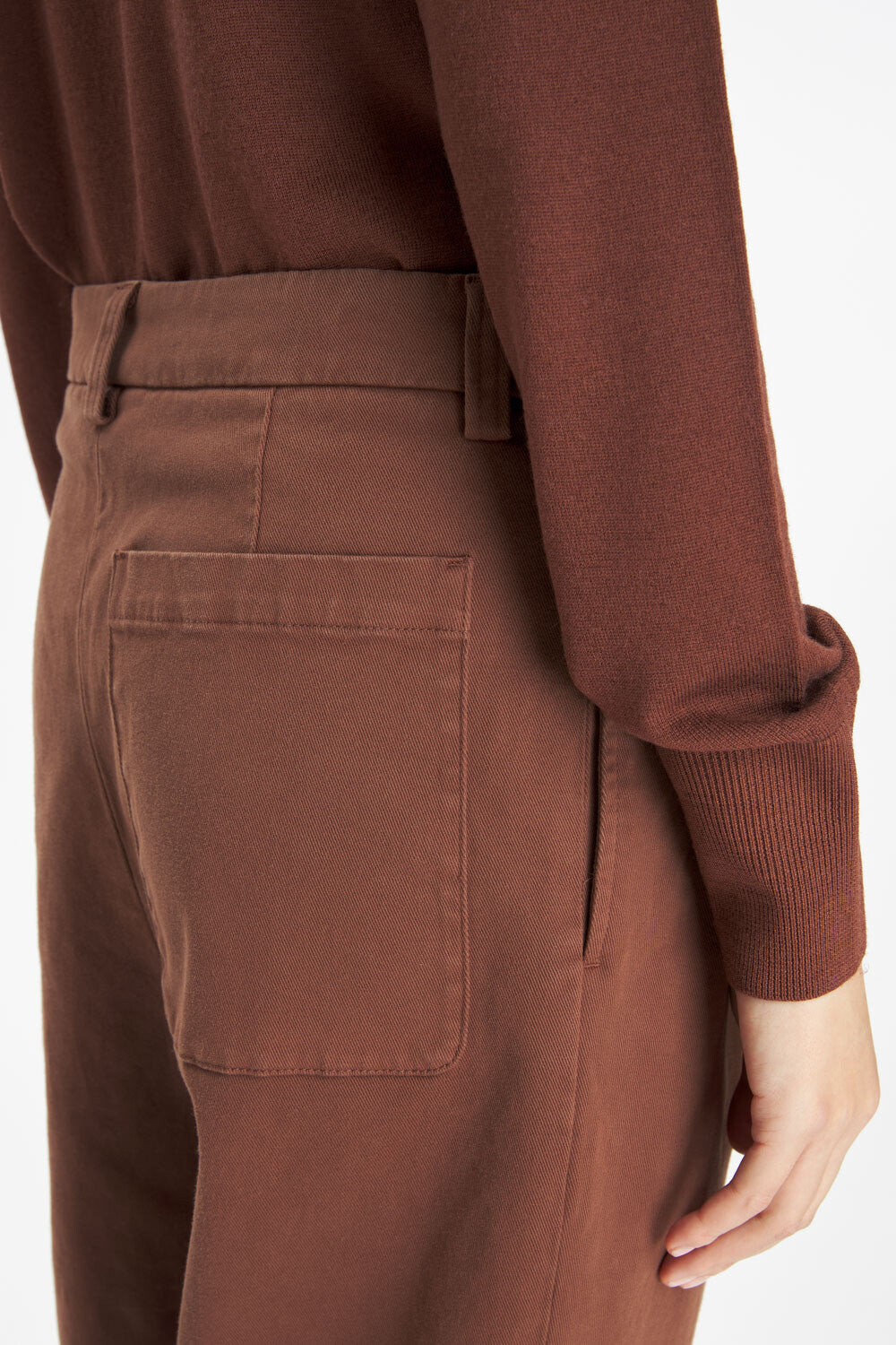 Close-up of a person wearing brown trousers with a back pocket and a matching brown long-sleeve top, shown against a plain light background.