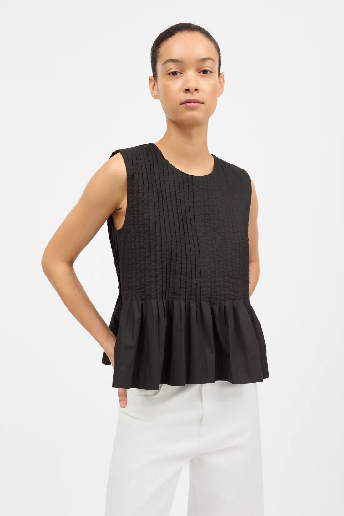 Woman wearing a black sleeveless top with a peplum waist on a white background