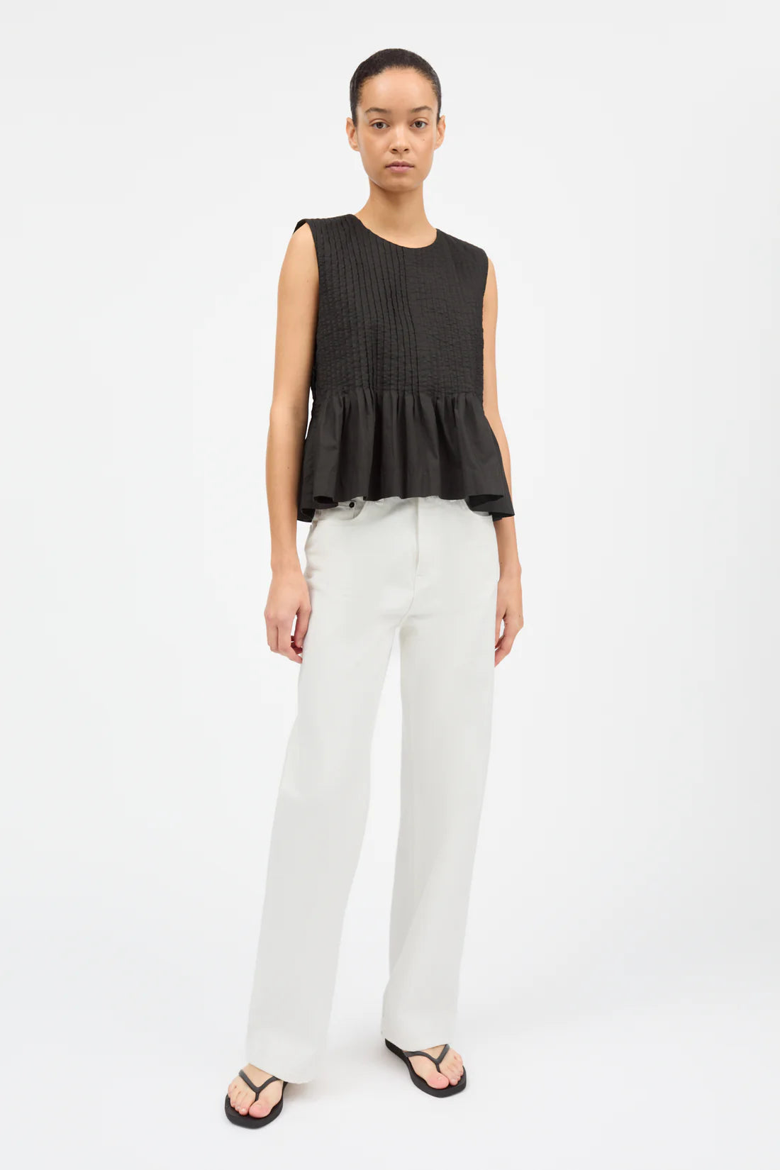 Woman wearing a black sleeveless top and white pants on a white background