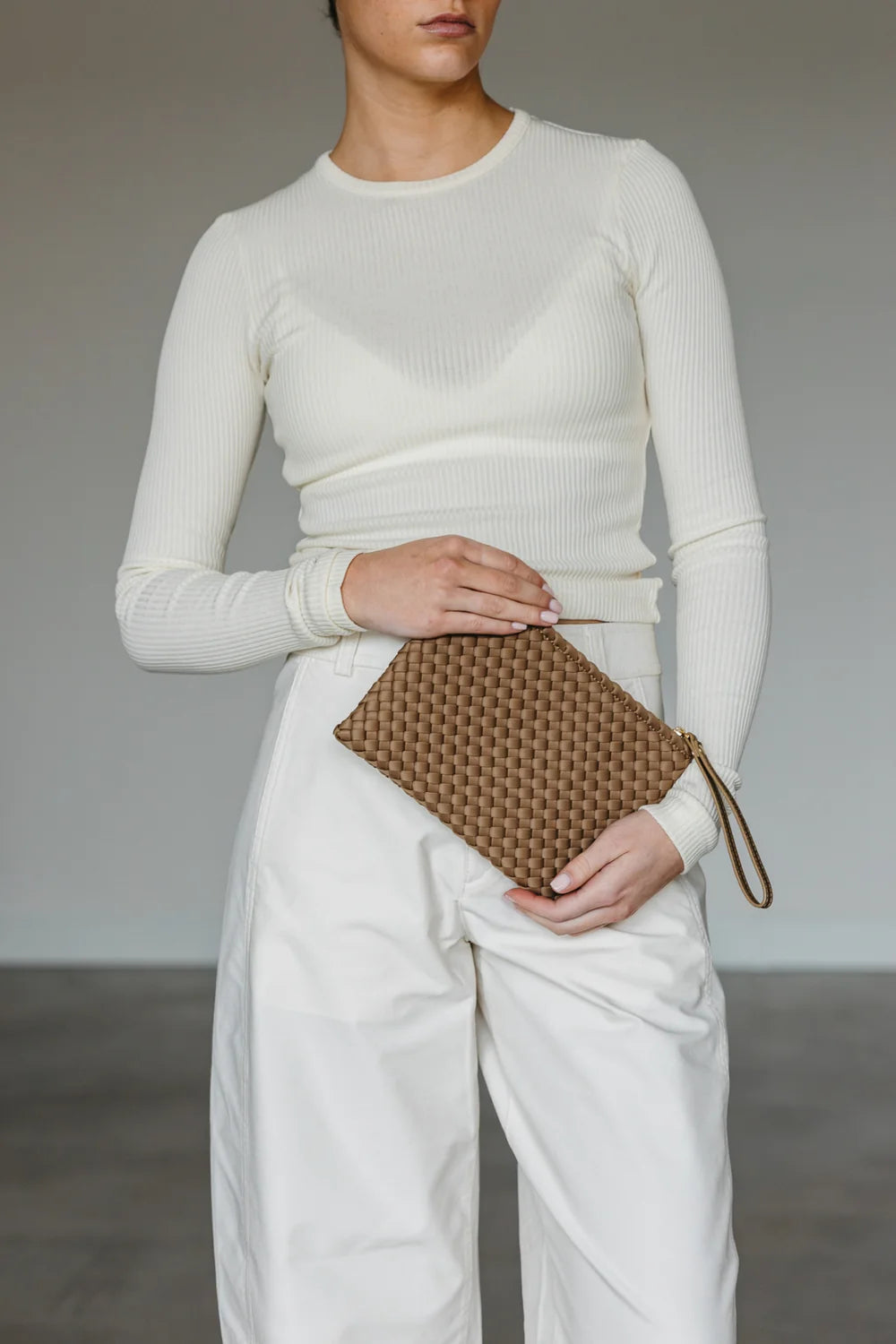Person wearing a white outfit holding a brown clutch against a neutral background