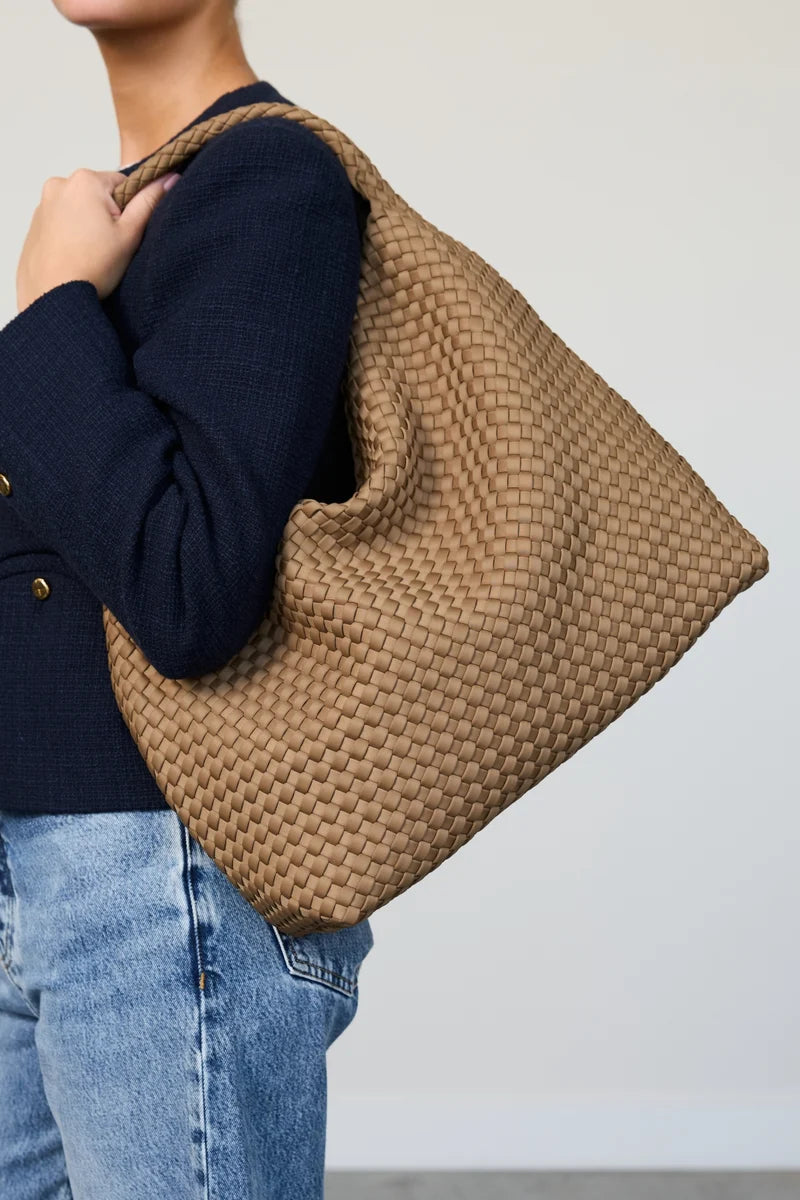 Person holding a woven brown bag against a plain background