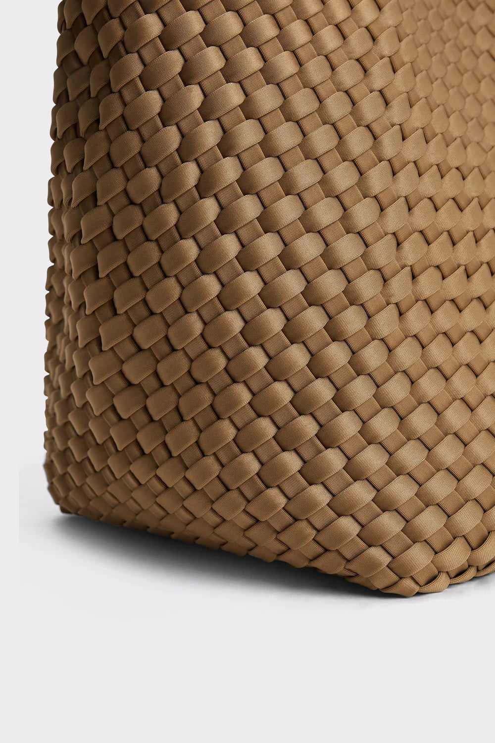 Close-up of a woven leather bag corner in a warm tan-brown color, showing the detailed basketweave texture against a light gray background.