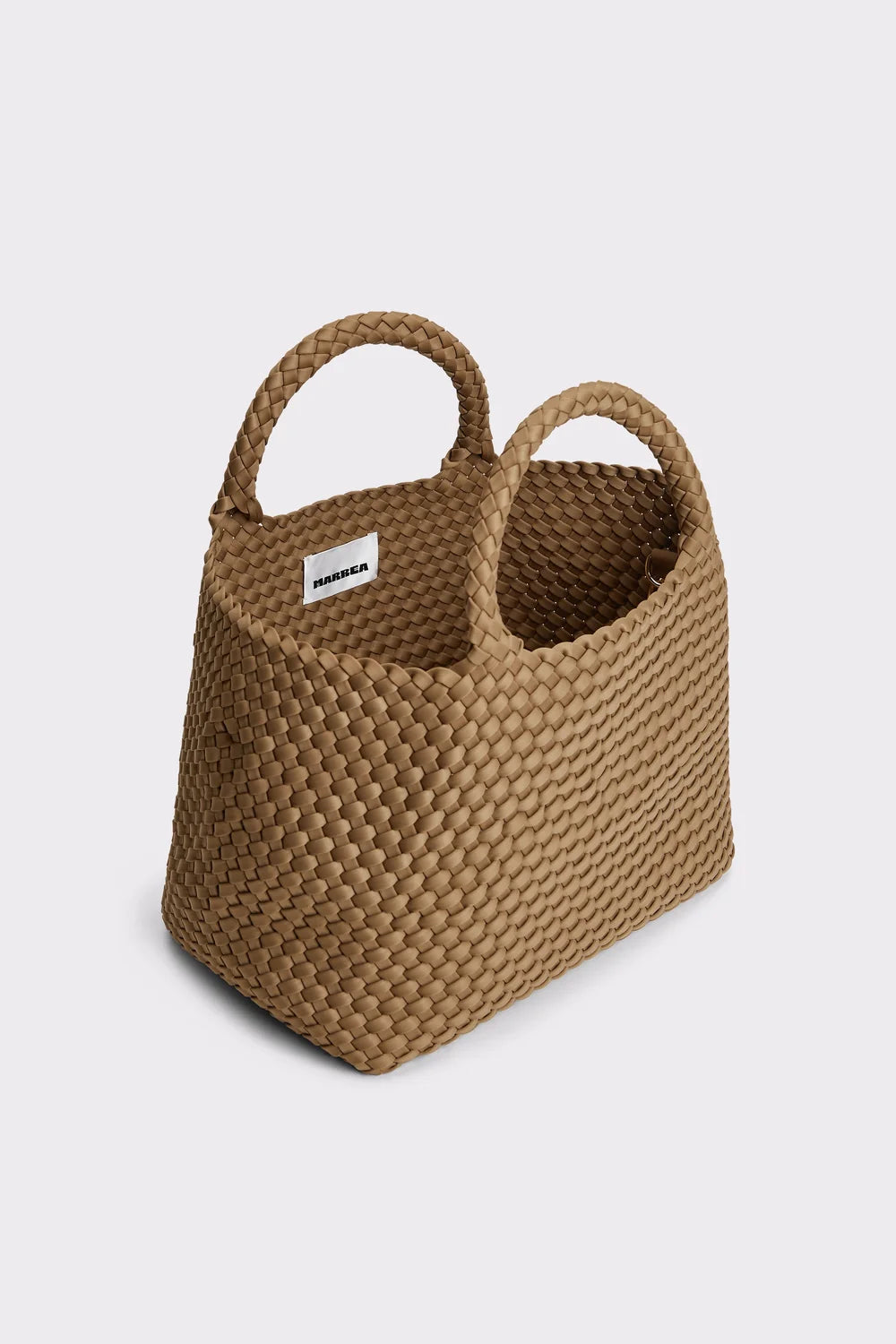 A woven straw tote bag with two top handles, shown on a light gray background. The bag has a small white brand tag on the side.