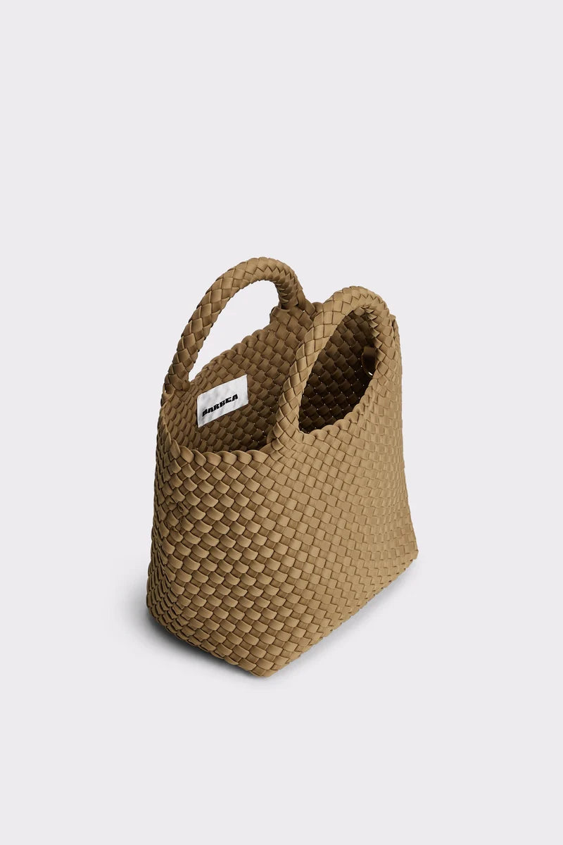 A woven straw tote bag in a light tan color, featuring two integrated top handles and a small white brand label on the side, set against a plain light gray background.