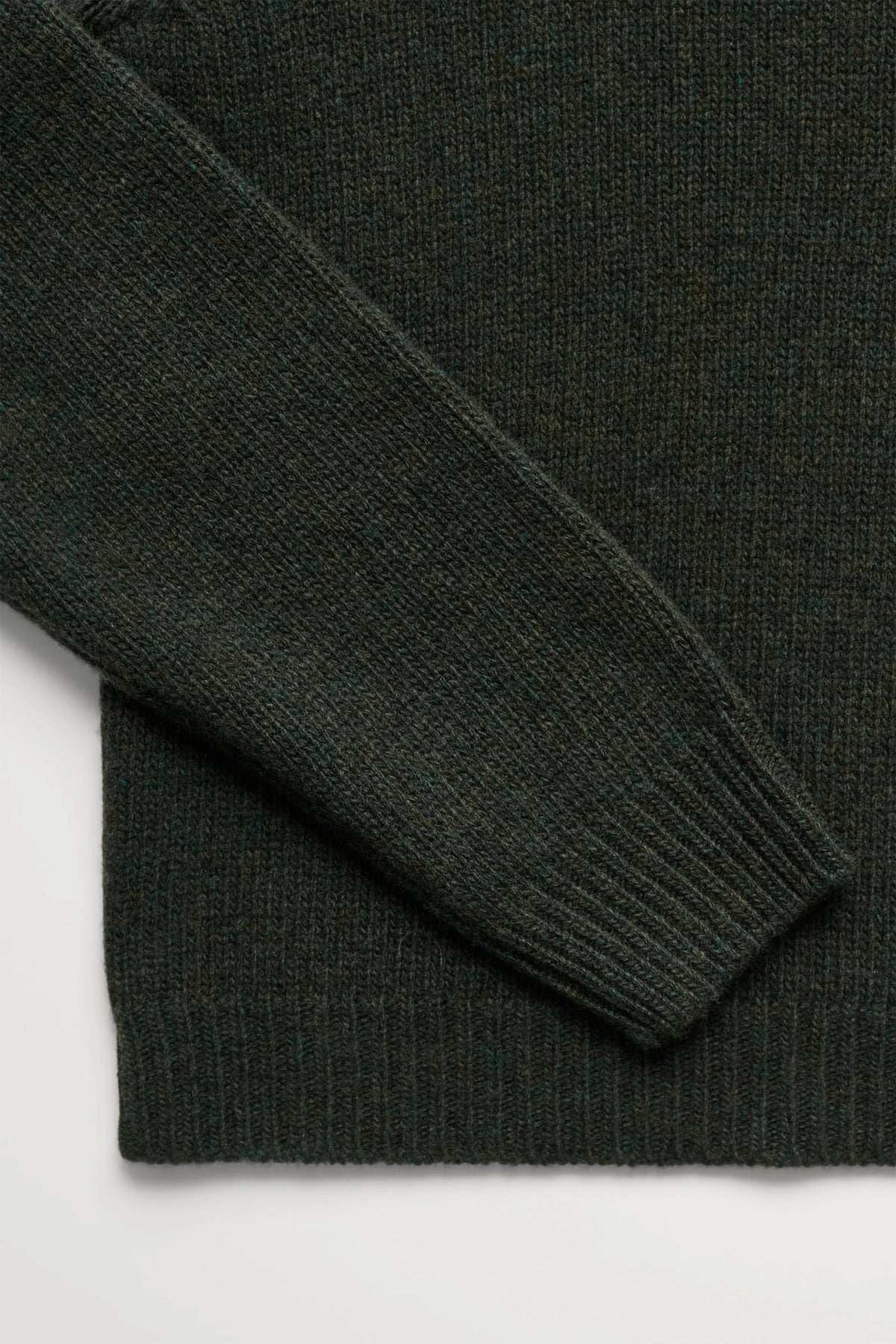 Close-up of a dark forest green knit sweater showing the ribbed cuff and sleeve against a light gray background.