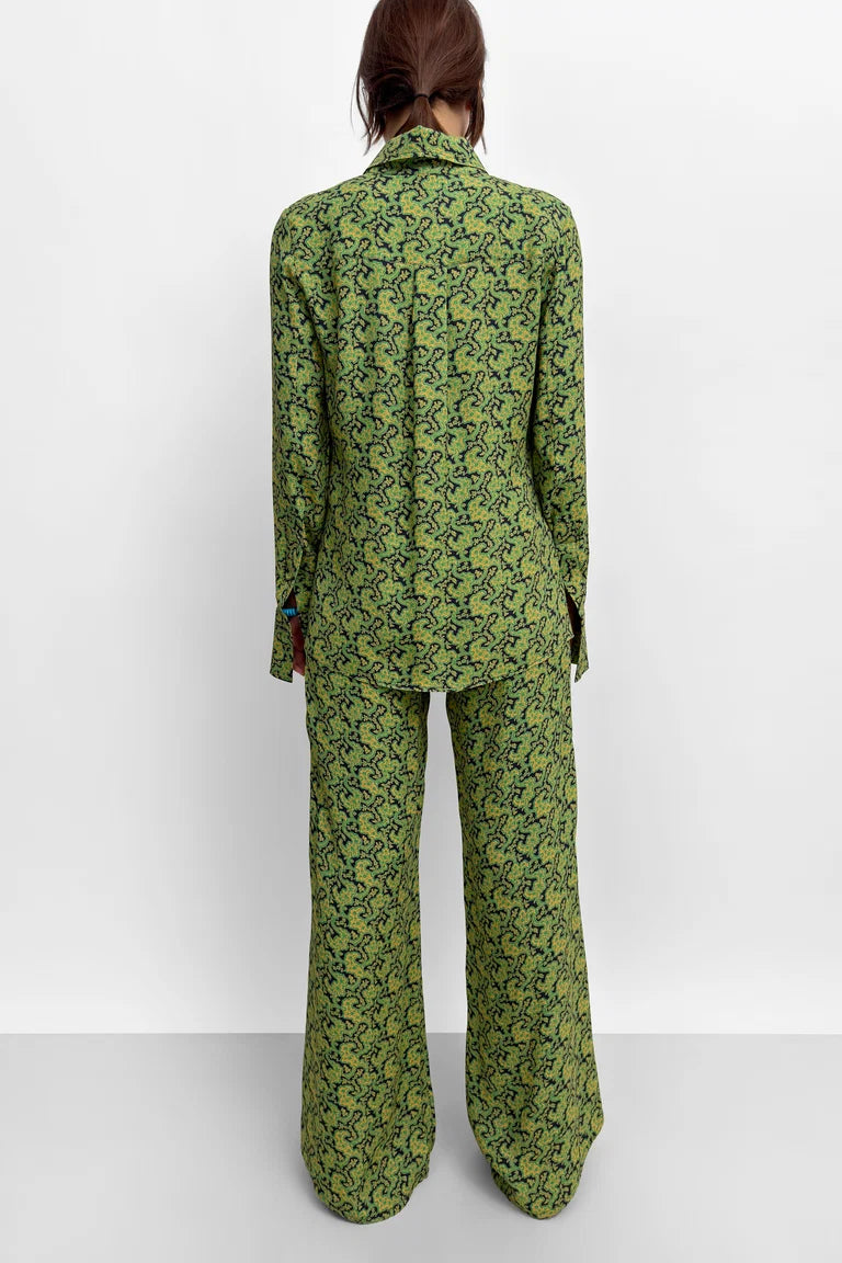A model viewed from the back wearing a matching green and black patterned blazer and wide-leg trousers set against a plain white studio background.