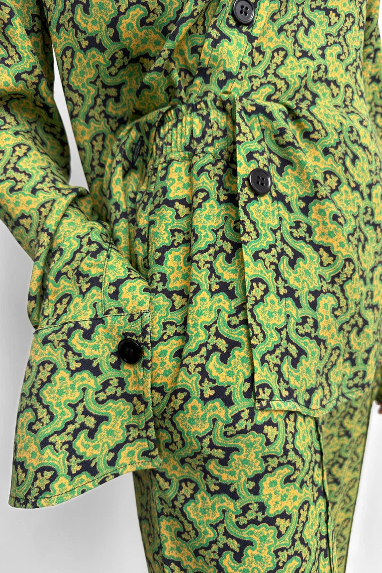 Close-up of a green and yellow abstract patterned garment with black buttons, shown on a mannequin or dress form against a plain light background.