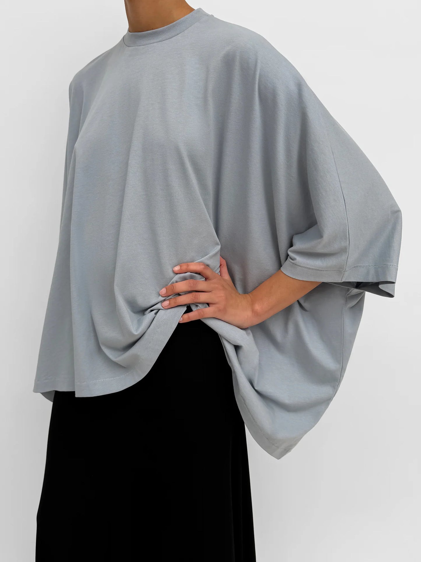 Person wearing a light gray oversized top with a plain background