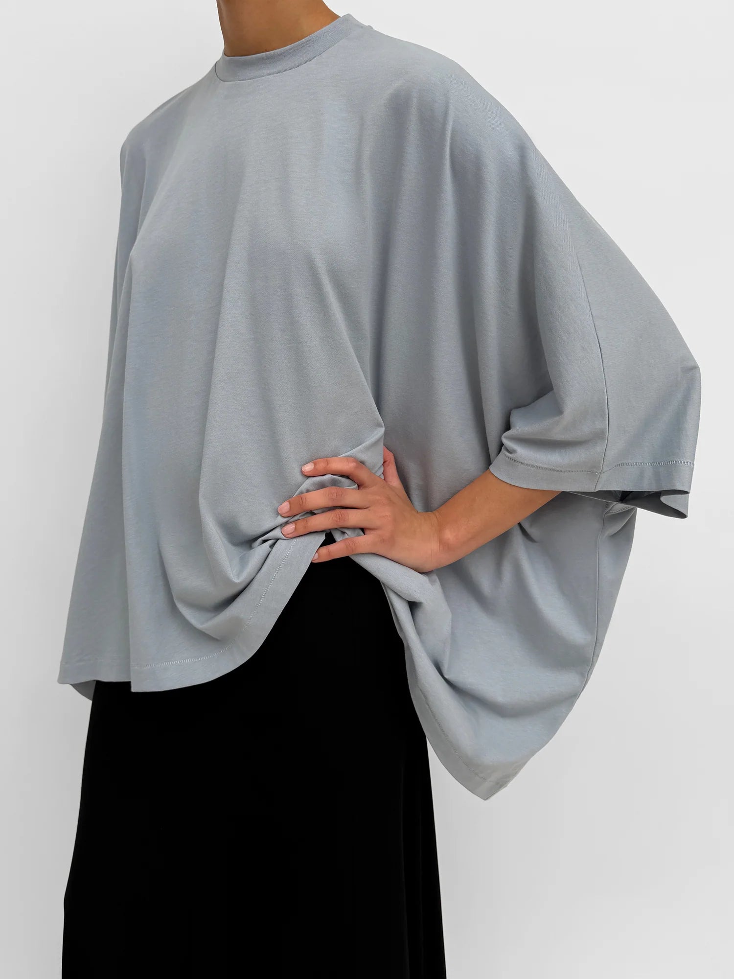 Person wearing a light gray oversized top with a plain background