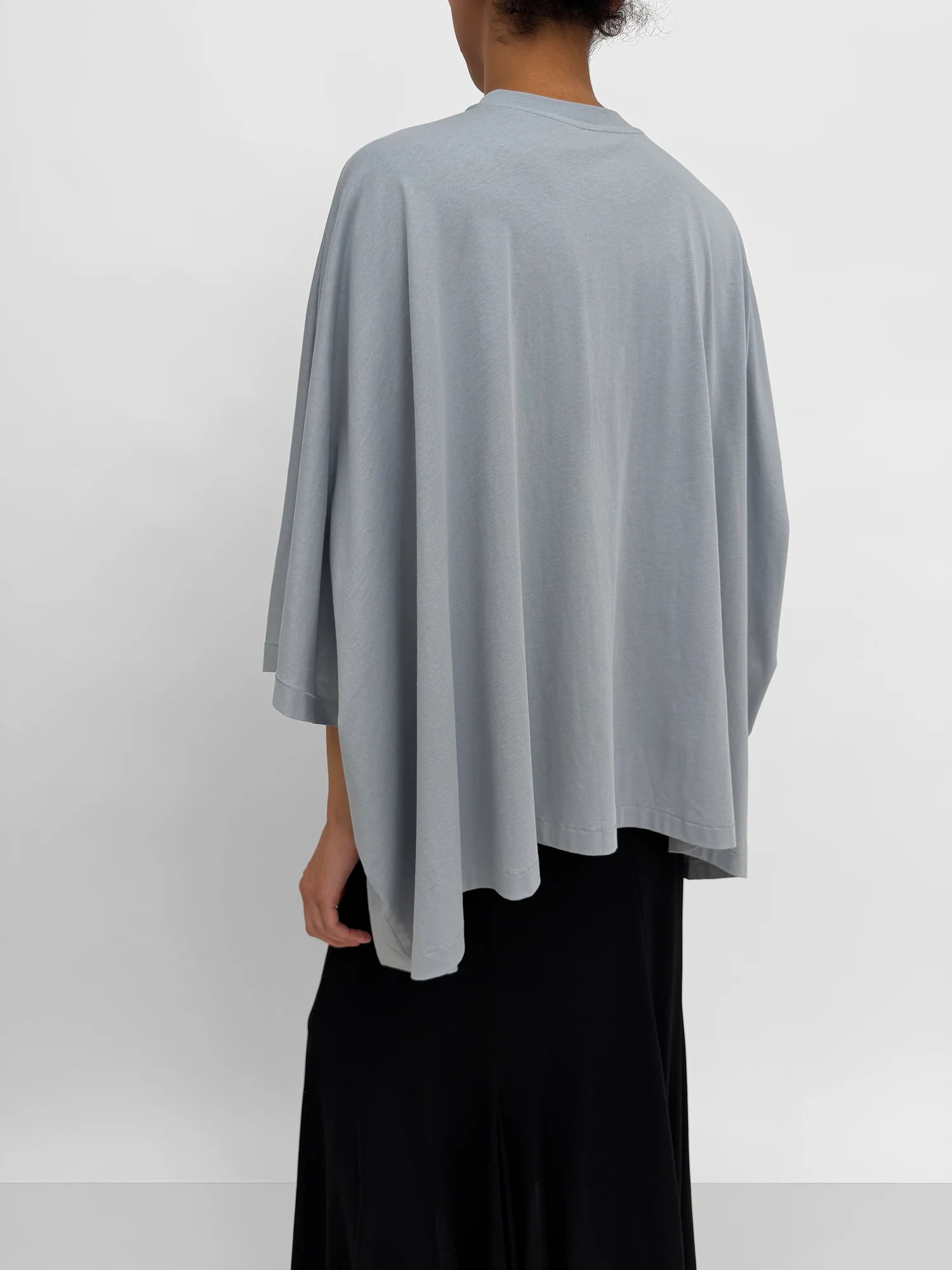 Person wearing a light gray poncho over a black outfit on a white background