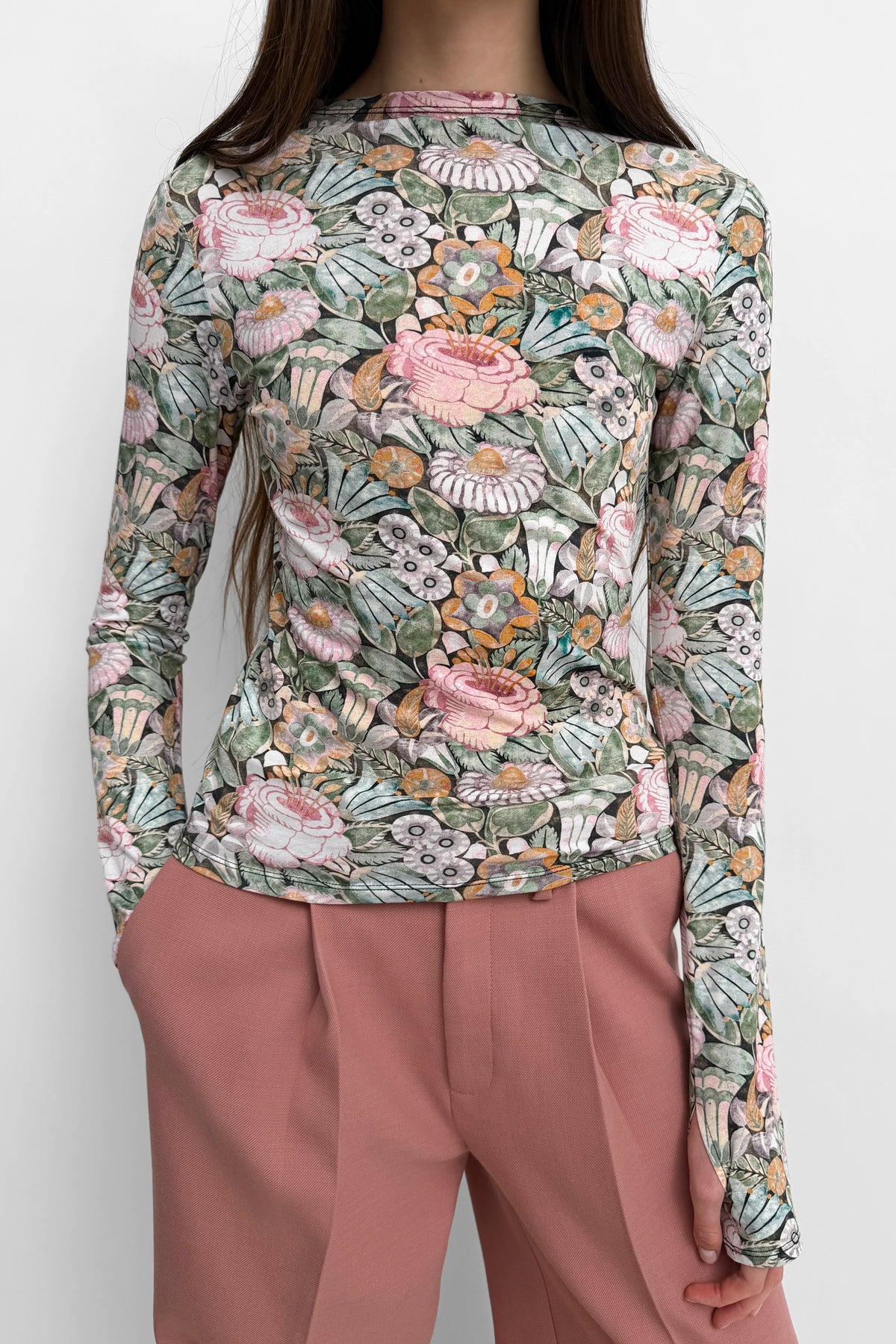 Person wearing a long-sleeve floral top and pink pants on a white background