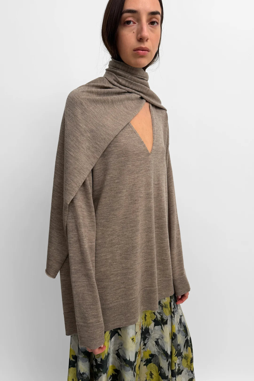 A model wearing a taupe-brown draped knit top with a keyhole cutout and a floral print skirt, photographed against a plain light gray background.